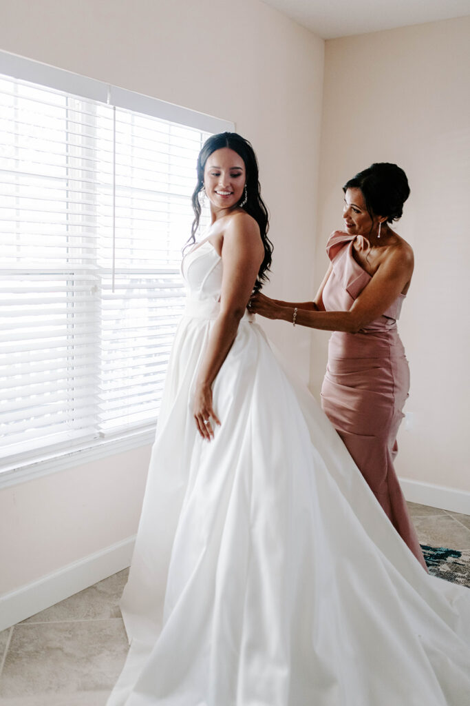 mother helps bride get into her wedding dress