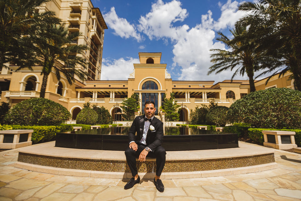 Groom sitting in front of fountain with building in the background